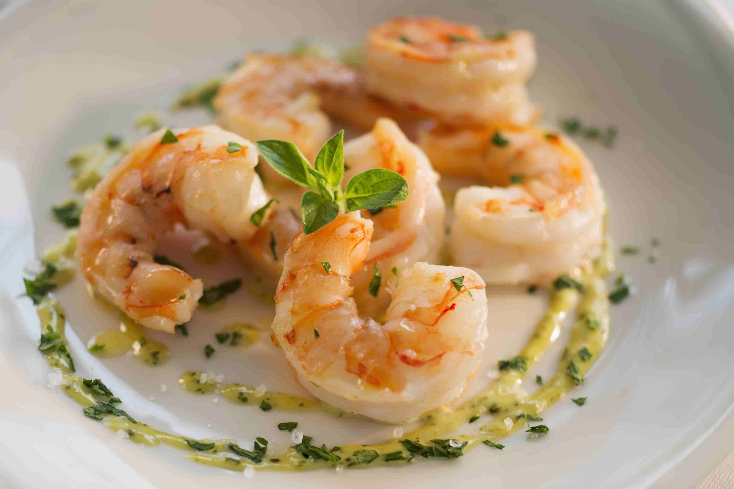 Pan-seared prawns with herb oil on white china